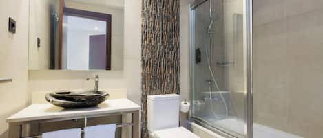A modern bathroom with a glass shower enclosure, a white sink with a unique basin, and a toilet with a vertical tile backsplash.