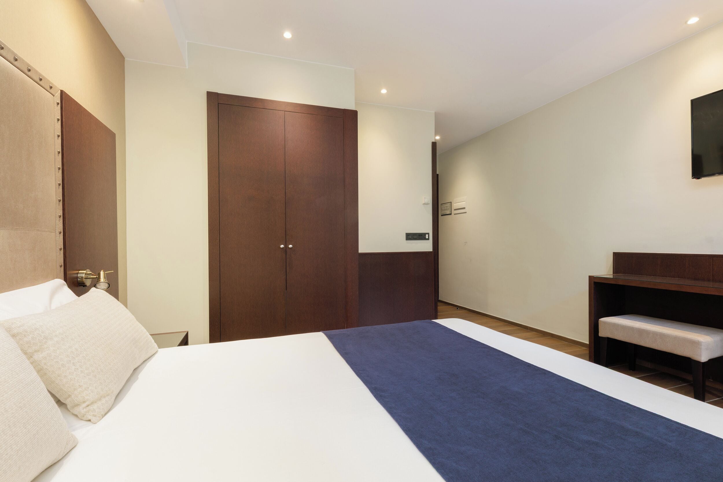 A hotel room with a bed, a wardrobe, a desk, and a mirror.