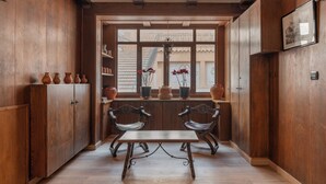 Interior de madera con una ventana, dos sillas, una mesa y estantes con cerámica.