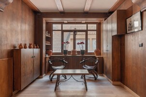 Interior de madera con una ventana, dos sillas, una mesa y estantes con cerámica.