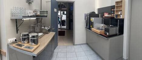 A compact kitchen area with a sink, stove, and various kitchen utensils. There is a small refrigerator and a shelf with cups and plates.