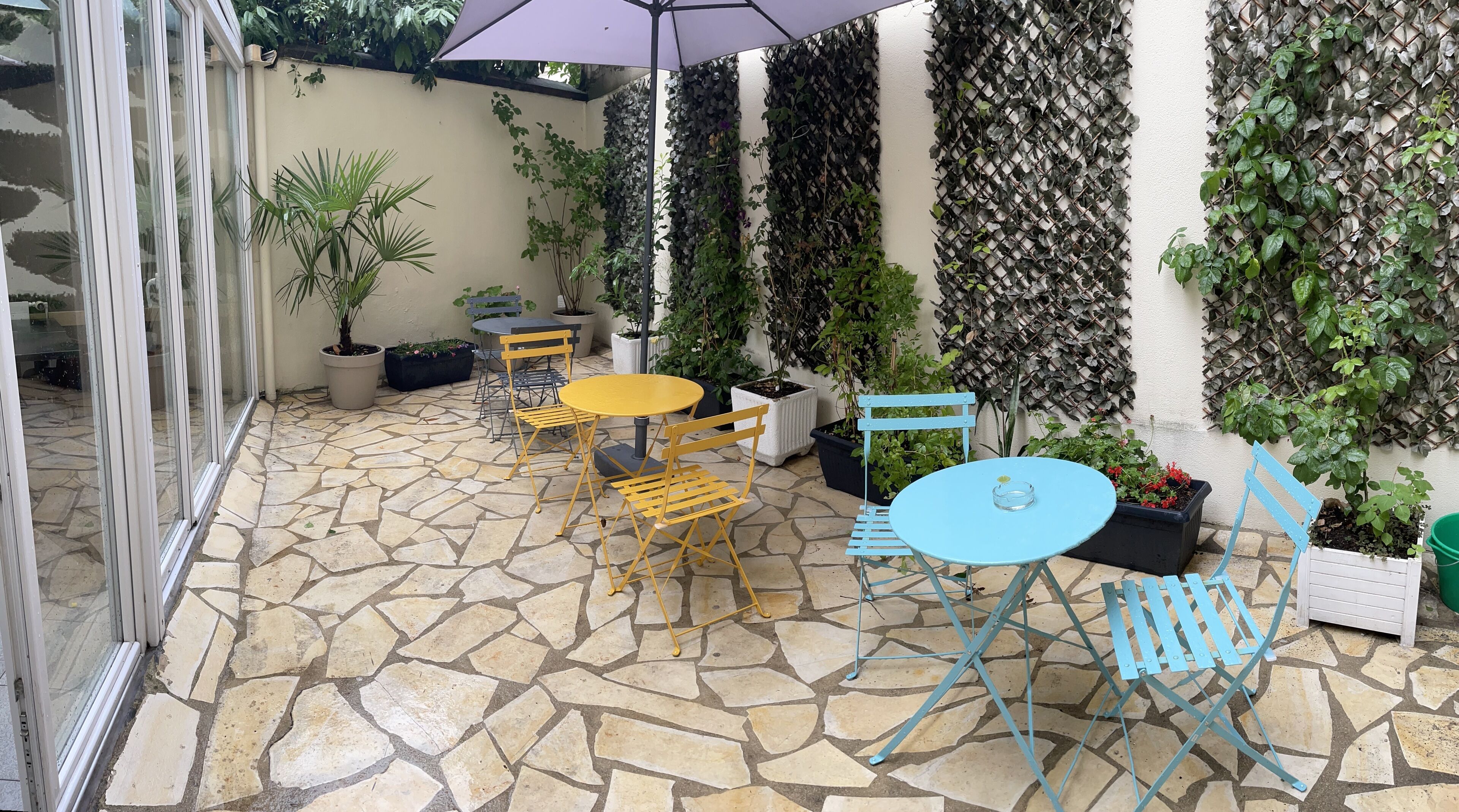 Une terrasse extérieure avec un sol en pierre, des meubles de jardin jaunes et bleus, et des plantes en pot.