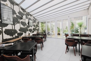 A restaurant with indoor and outdoor seating, a patterned wall, and a view of greenery.