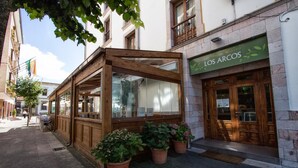 A wooden structure with large windows, potted plants, and a storefront with a green sign.