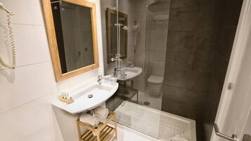 Een moderne badkamer met een douche met glazen wand, een wit wastafel en een houten plank.