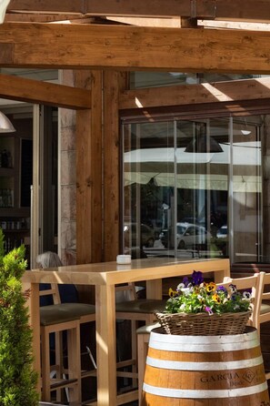 Un espacio de estar al aire libre con muebles de madera, incluyendo una mesa y sillas, una cesta de mimbre con flores y un barril de madera con texto.