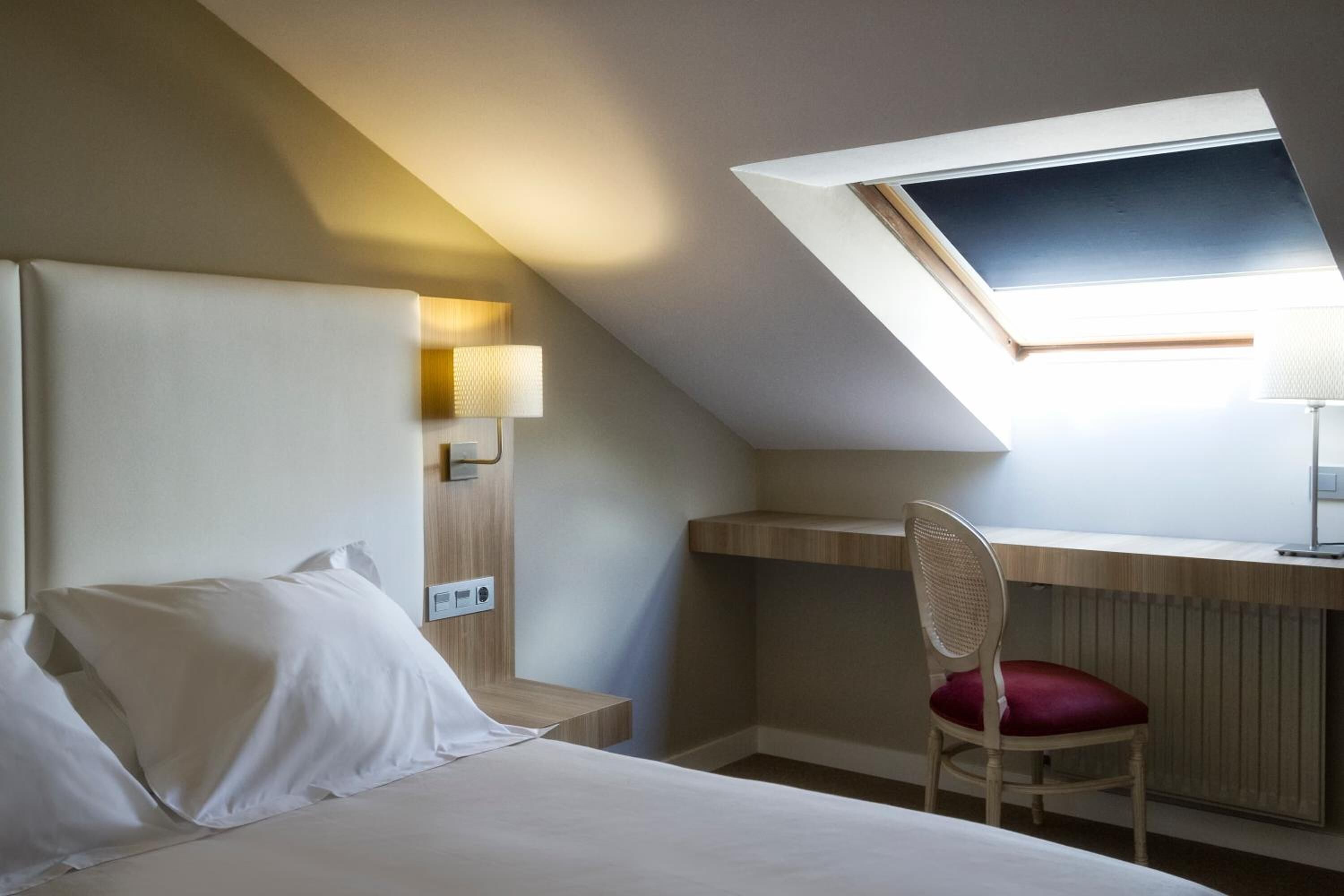 Habitación de hotel con cama, escritorio, silla y tragaluz.