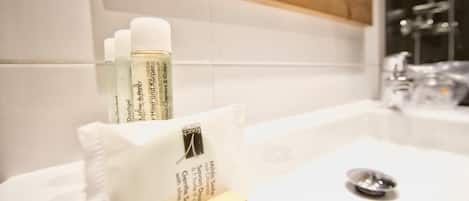 Un baño con un lavamanos blanco, un espejo y artículos de aseo, incluyendo una botella de jabón y una caja de pañuelos.