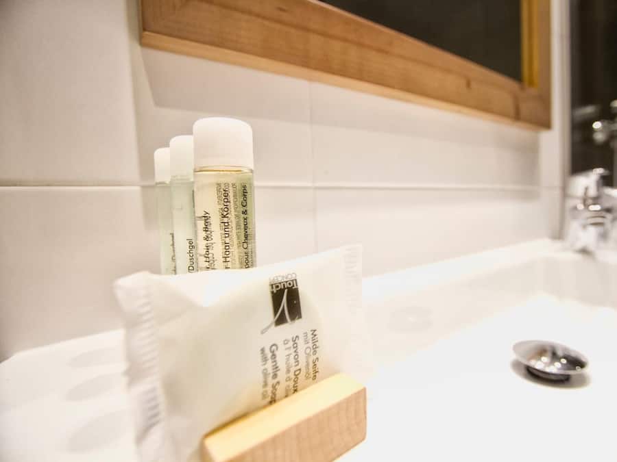 Un baño con un lavamanos blanco, un espejo y artículos de aseo, incluyendo una botella de jabón y una caja de pañuelos.