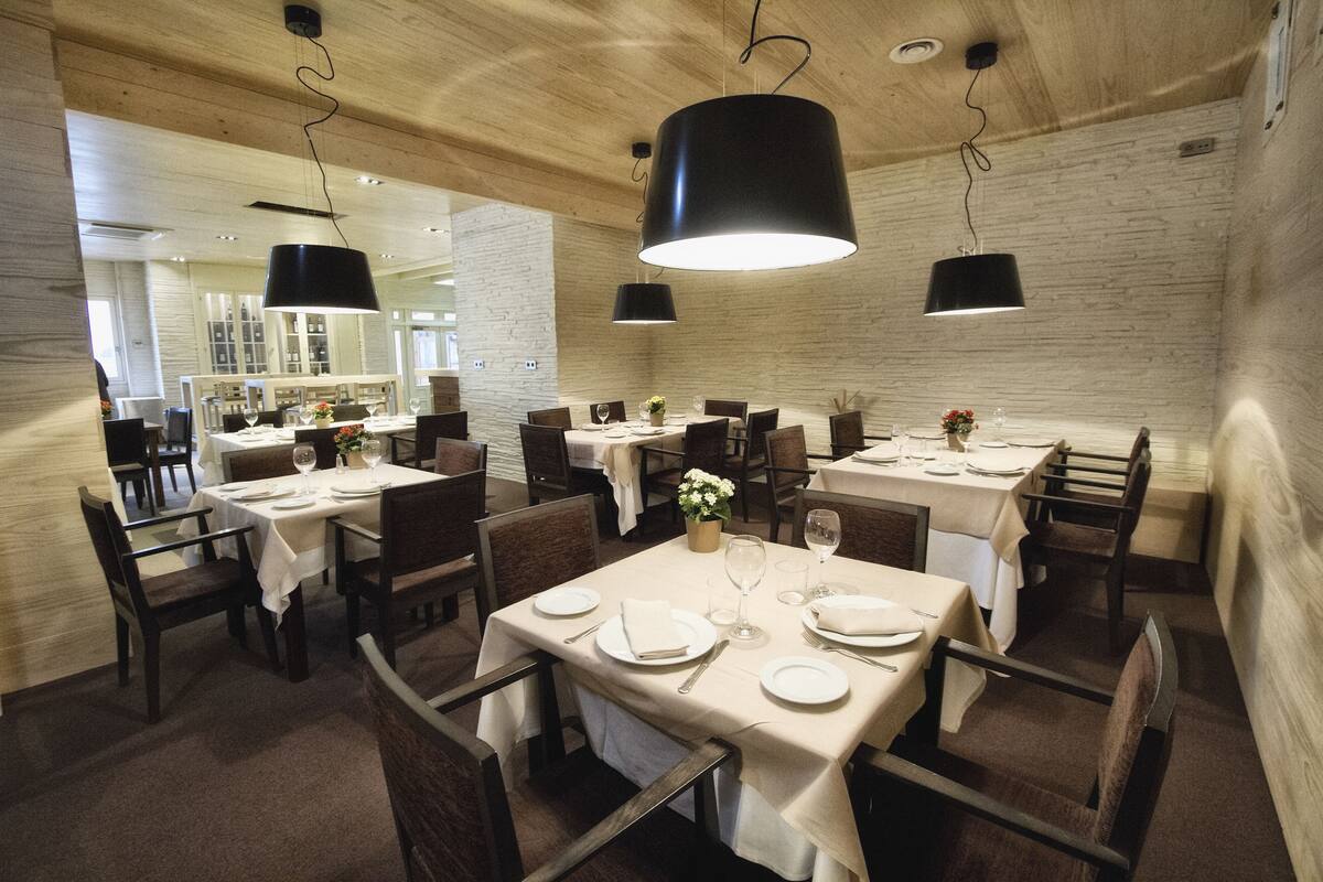 Un restaurante con varias mesas, sillas de madera oscura y lámparas colgantes negras.