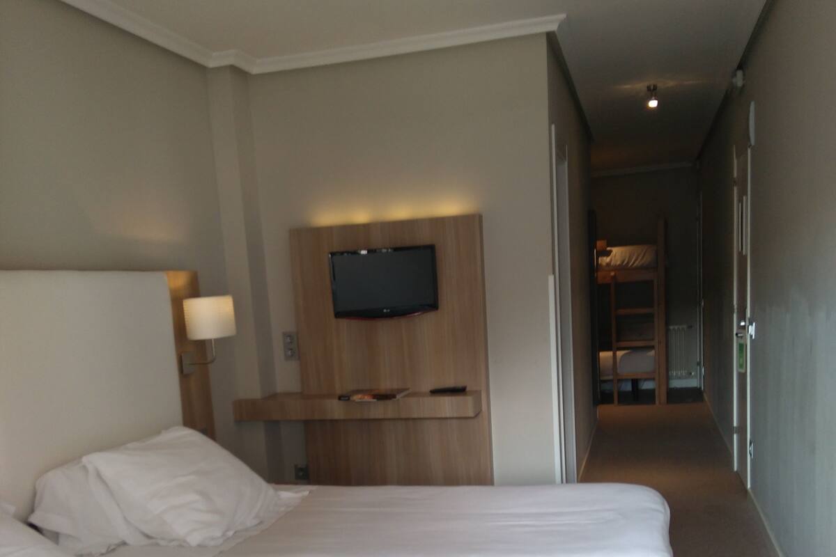 Una habitación de hotel con una cama grande, un televisor montado en la pared y una mesita de noche con lámpara.