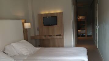 Ein Hotelzimmer mit einem großen Bett, einem an der Wand befestigten Fernseher und einem Nachttisch mit Lampe.