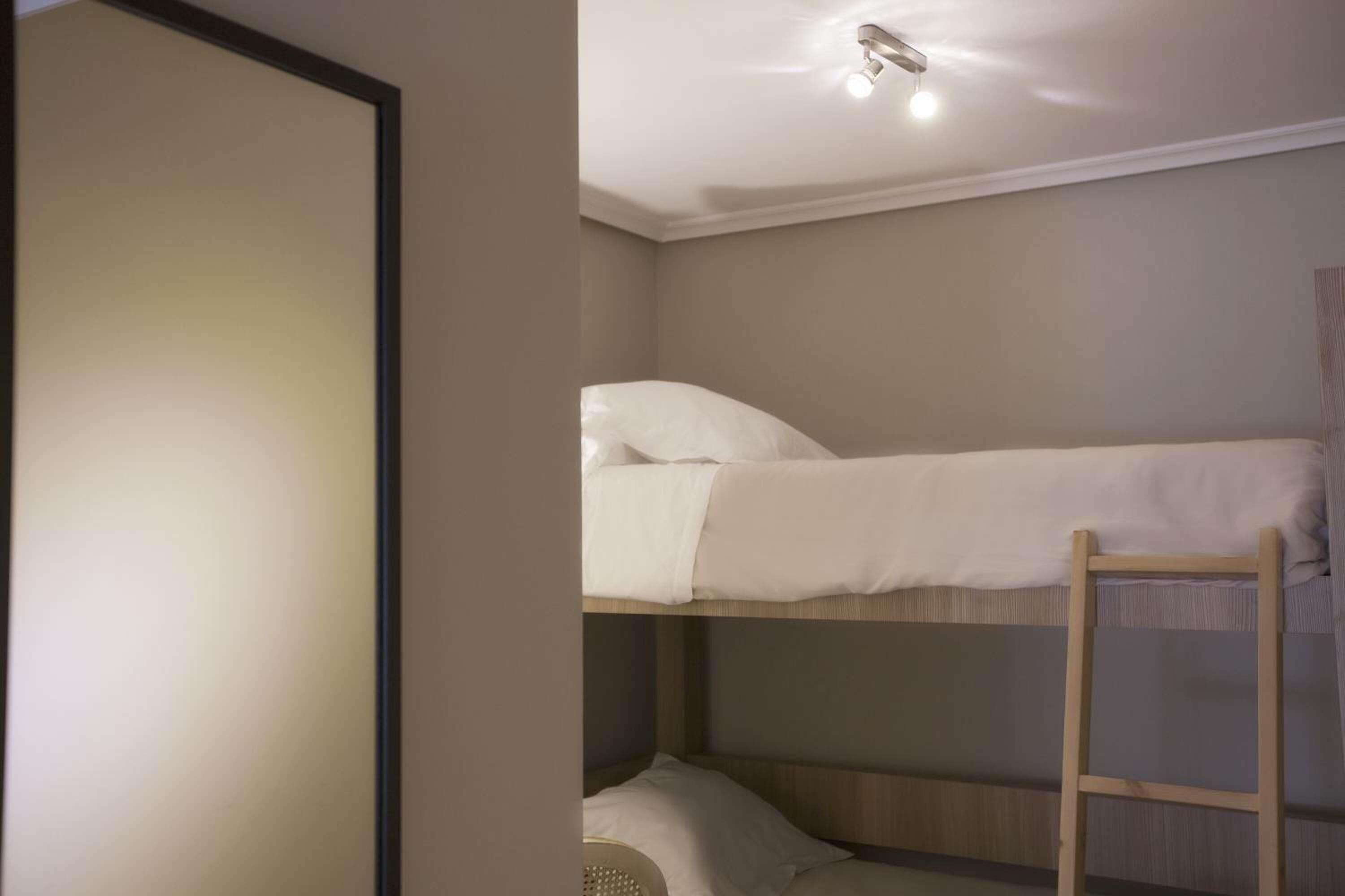 A bunk bed with a ladder, a ceiling light, and a wall with a textured pattern.