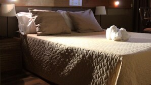 Une chambre d’hôtel avec un grand lit, deux lampes fixées au mur et deux œuvres d’art.