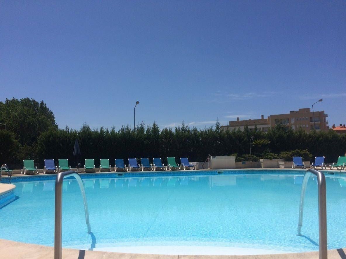 A swimming pool with blue water, surrounded by lounge chairs and a building in the background.
