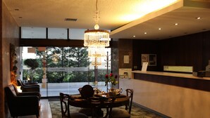 Un espace repas agrémenté d’un lustre, d’une table ronde et de chaises. On y trouve un comptoir d’accueil avec un ordinateur et un panneau affiché sur le mur.