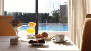 Une table de petit-déjeuner avec vue sur une piscine, un dessert servi dans un verre et un croissant.