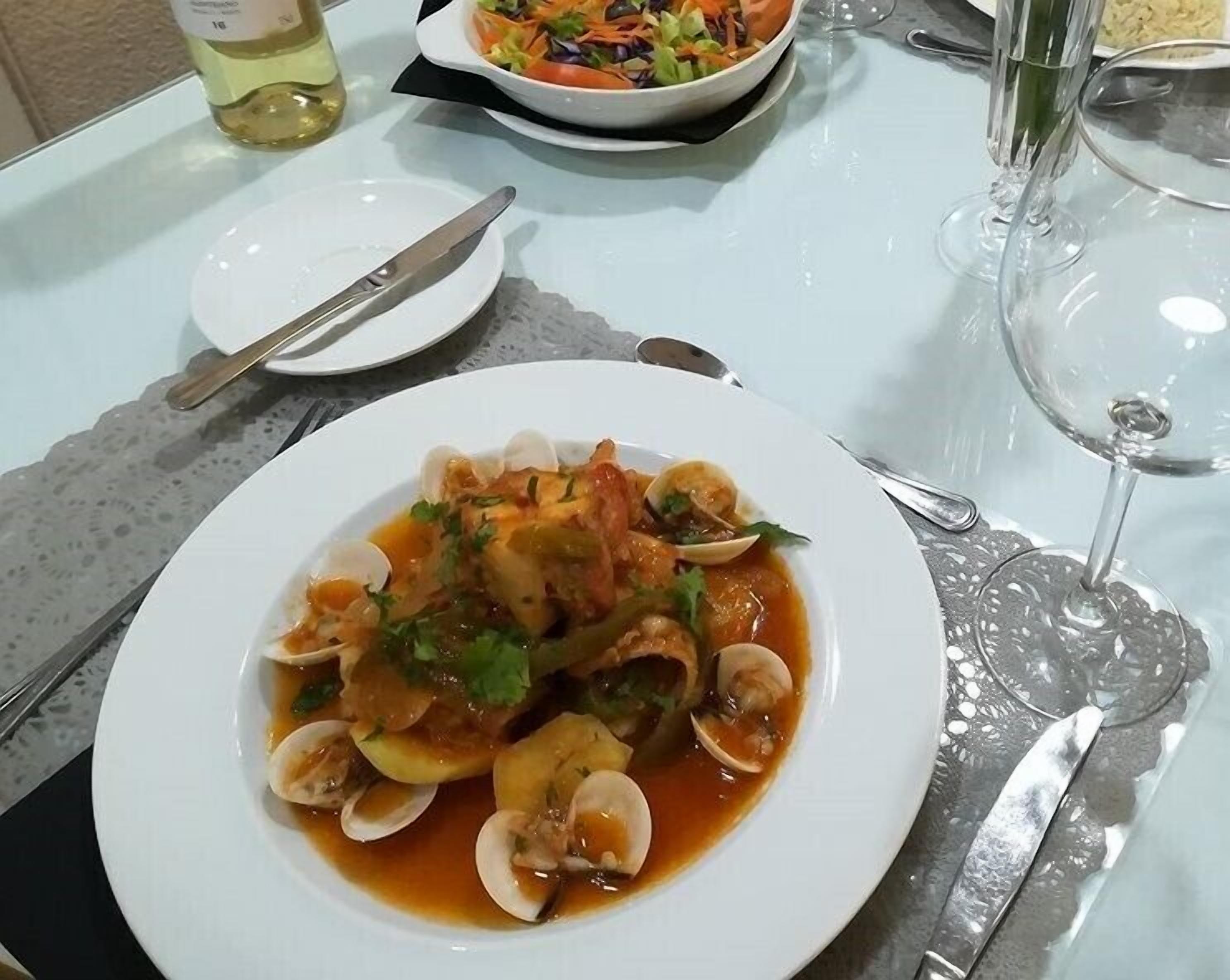 A dining table with a plate of seafood pasta, a bottle of white wine, and a glass of water.