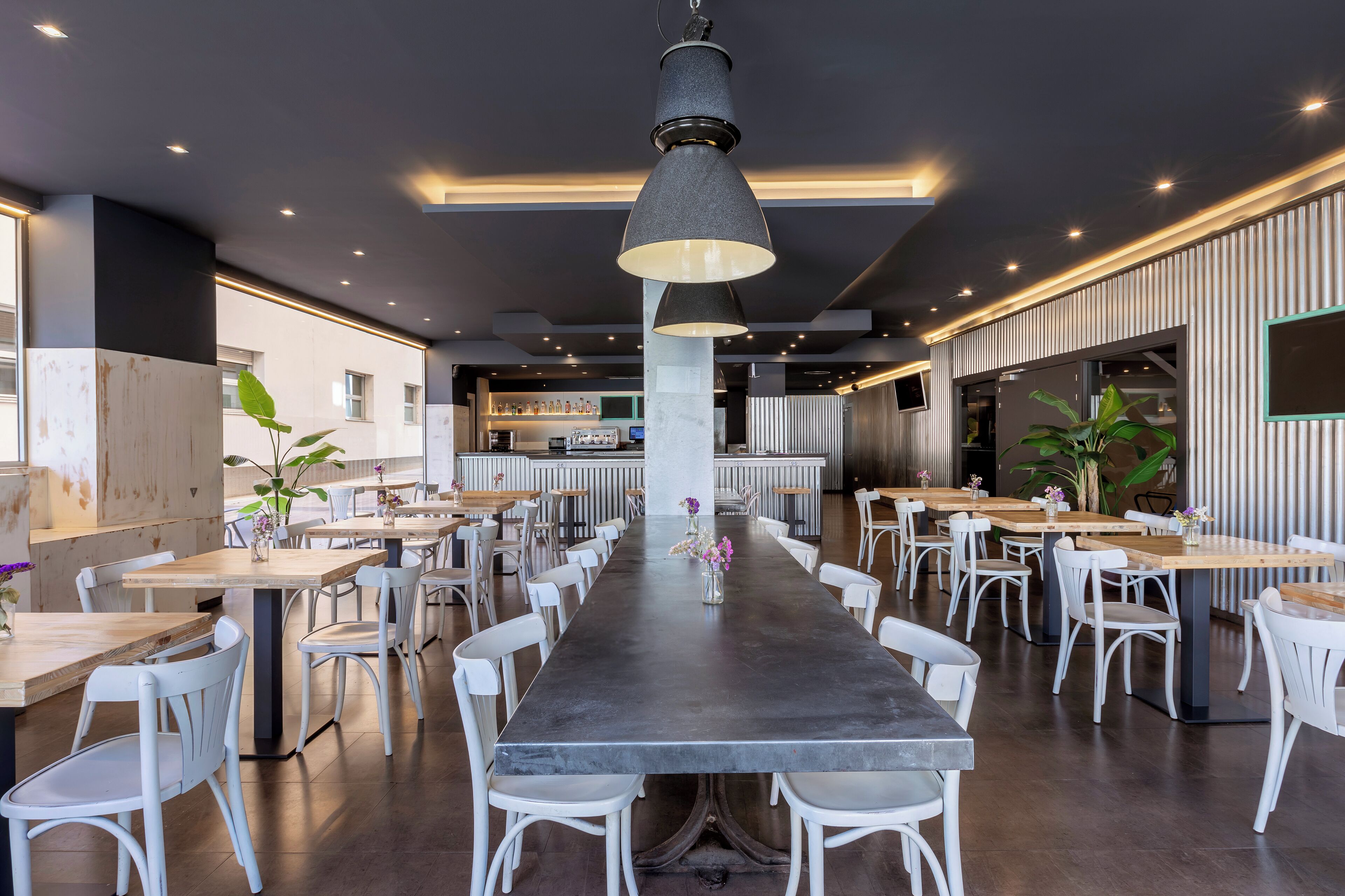 Un restaurante moderno con una larga mesa de comedor, sillas blancas e iluminación colgante.