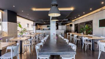 Un restaurante moderno con una larga mesa de comedor, sillas blancas e iluminación colgante.