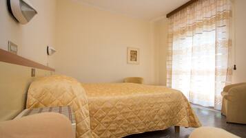 A hotel room with a bed, a chair, a wall-mounted light, and a window with curtains.