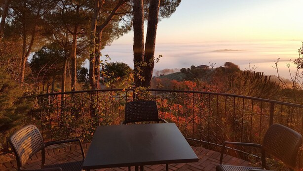 Una terraza con mesa y sillas, con vista a un paisaje boscoso y una casa distante.