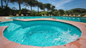 Piscina con múltiples carriles, rodeada de sillas de descanso y árboles.