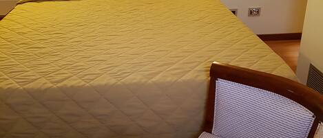 A neatly made bed with a wooden headboard, a wicker chair, and a wall-mounted light fixture.