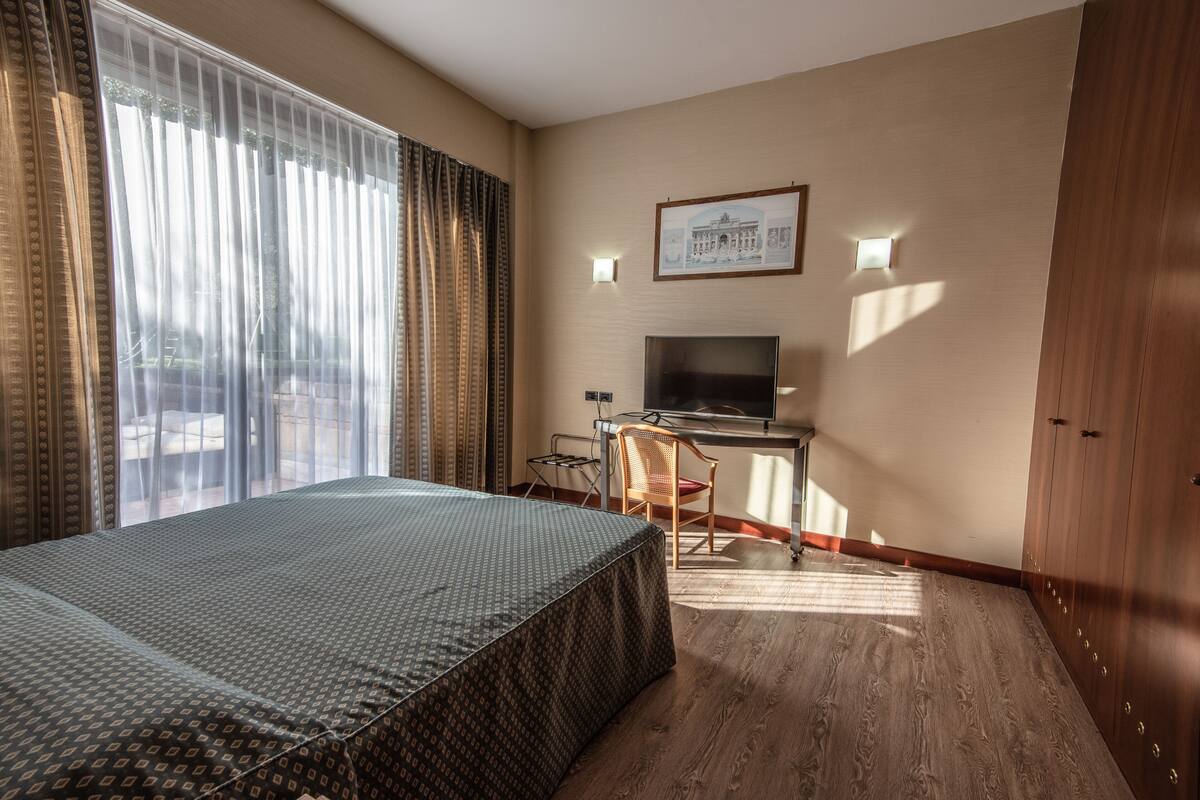Ein Hotelzimmer mit einem Bett, einem Schreibtisch, einem Sessel, einem Fernseher und einem gerahmten Bild an der Wand.