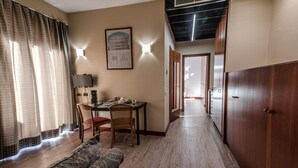 A hotel room with a wooden floor, a sofa, a dining table with chairs, a TV, and a framed picture on the wall. - Hotel Petra (Rome)