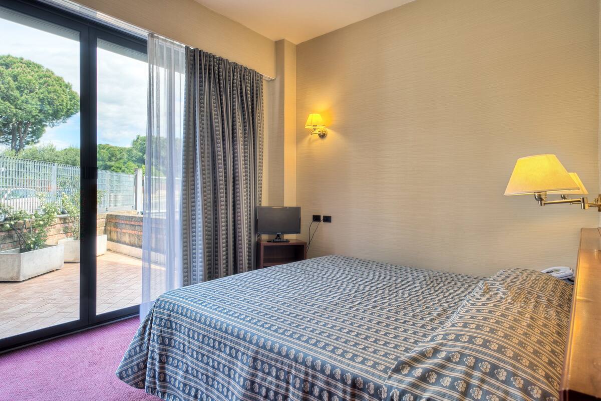 Ein Hotelzimmer mit Bett, Fernseher, Lampe und Blick ins Freie.