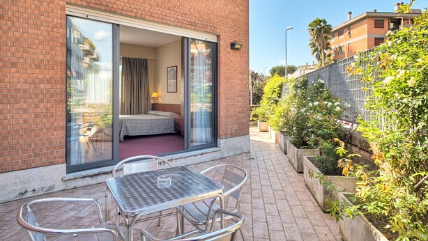 A hotel room with a sliding glass door leading to a balcony, a small table and chairs, and a bed with a view of the surrounding area. - Hotel Petra (Rome)