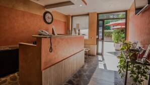 A reception desk with a clock, a phone, and a window with blinds. - Hotel Petra (Rome)