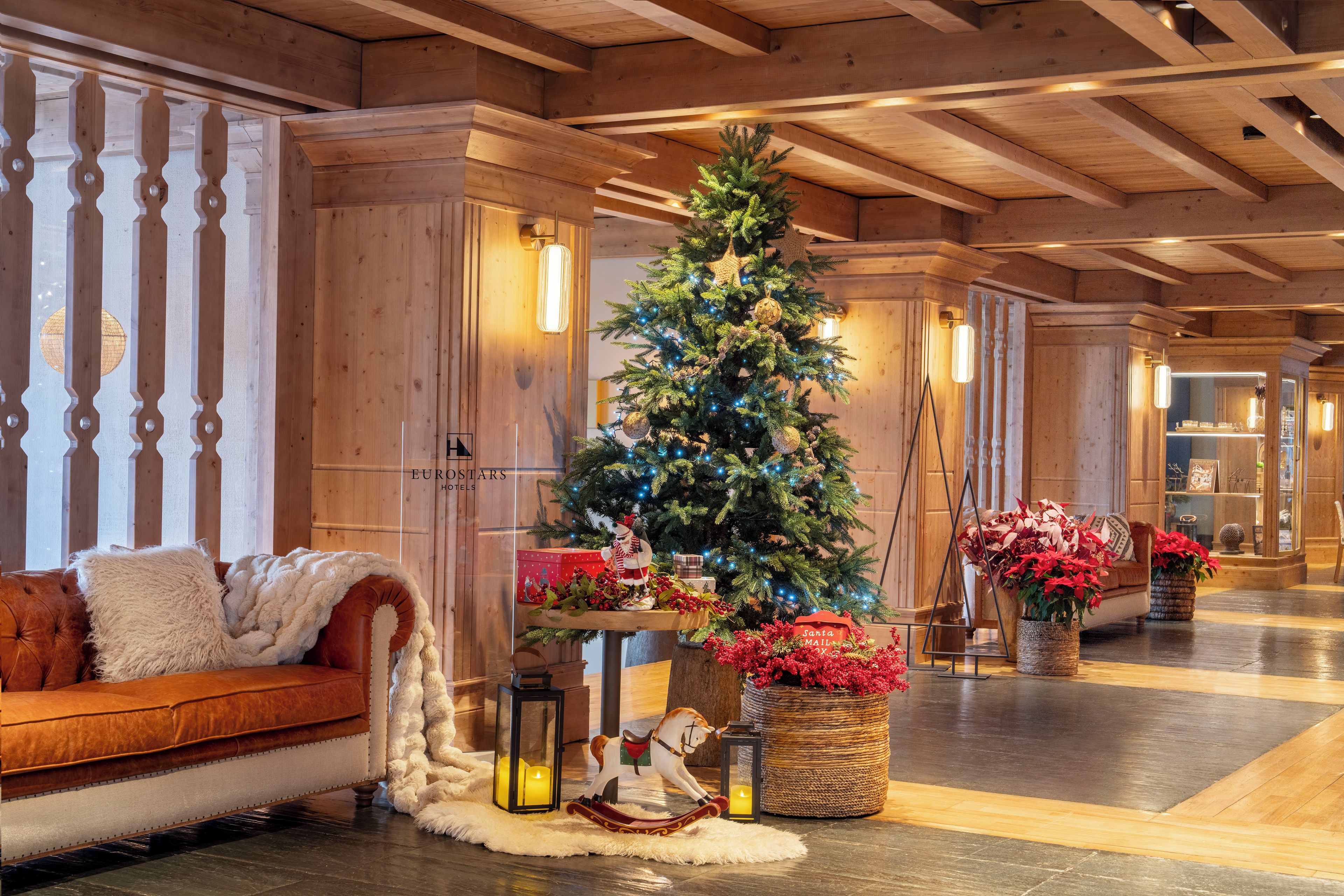 A cozy lobby with a wooden ceiling, a Christmas tree, a leather sofa, and a fireplace.