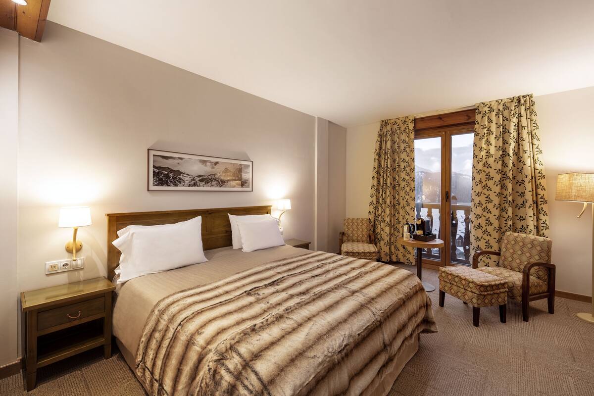 Une chambre d’hôtel avec un grand lit, deux tables de chevet avec des lampes, une chaise, une fenêtre avec des rideaux et un tableau encadré au mur.