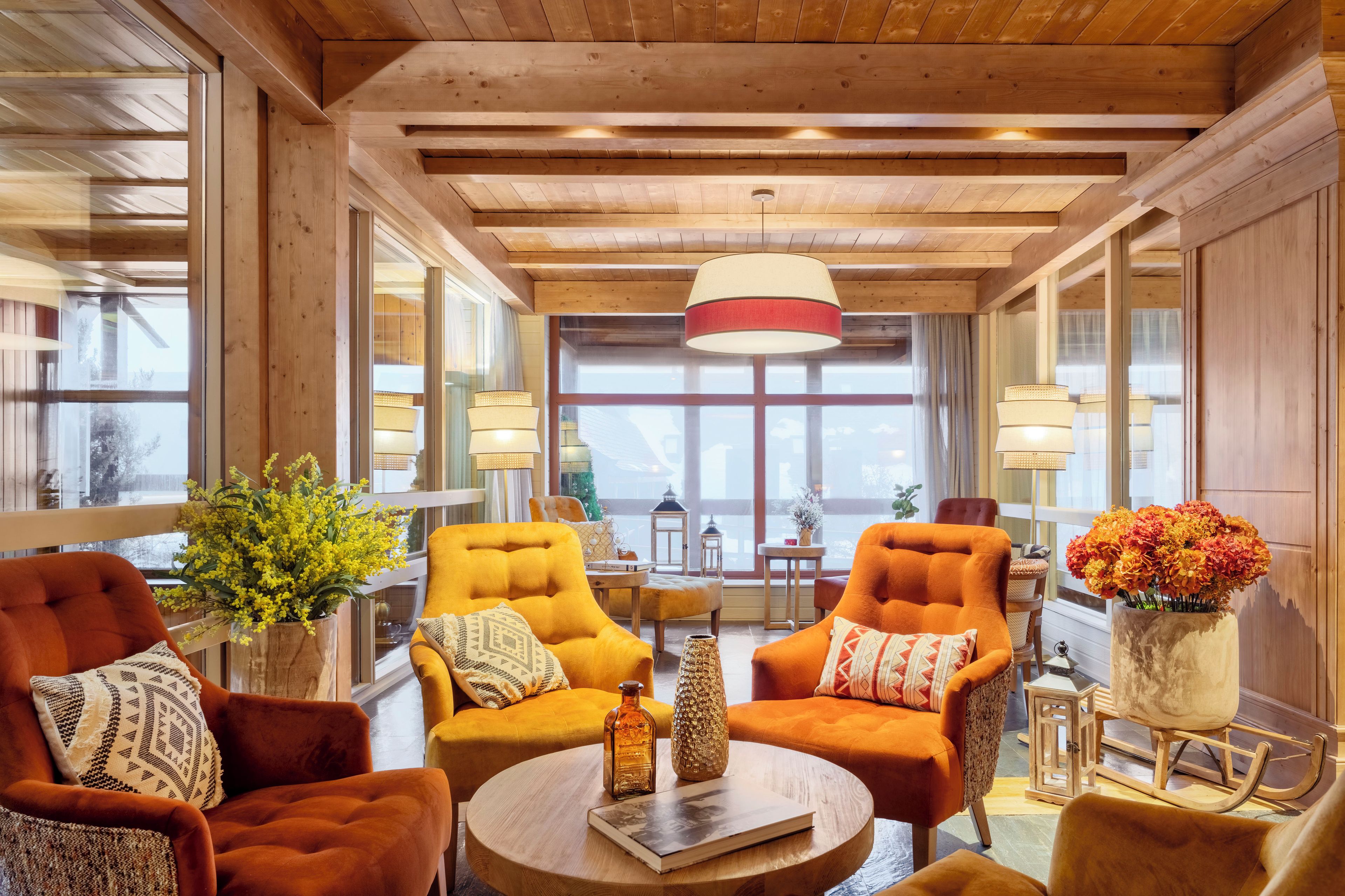Una habitación con vigas de madera en el techo, ventanas amplias y sillones tapizados en color naranja.