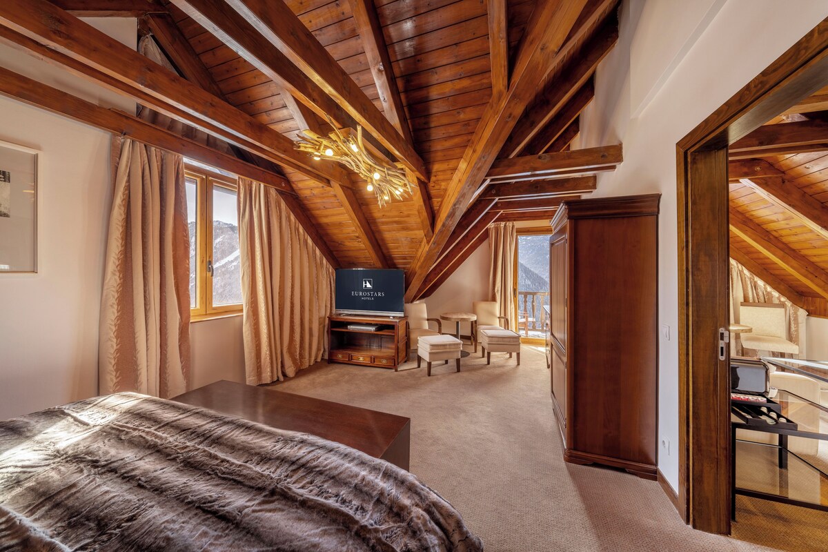 Un dormitorio con techo de madera, una cama, un televisor y una zona de escritorio con una silla y una lámpara.