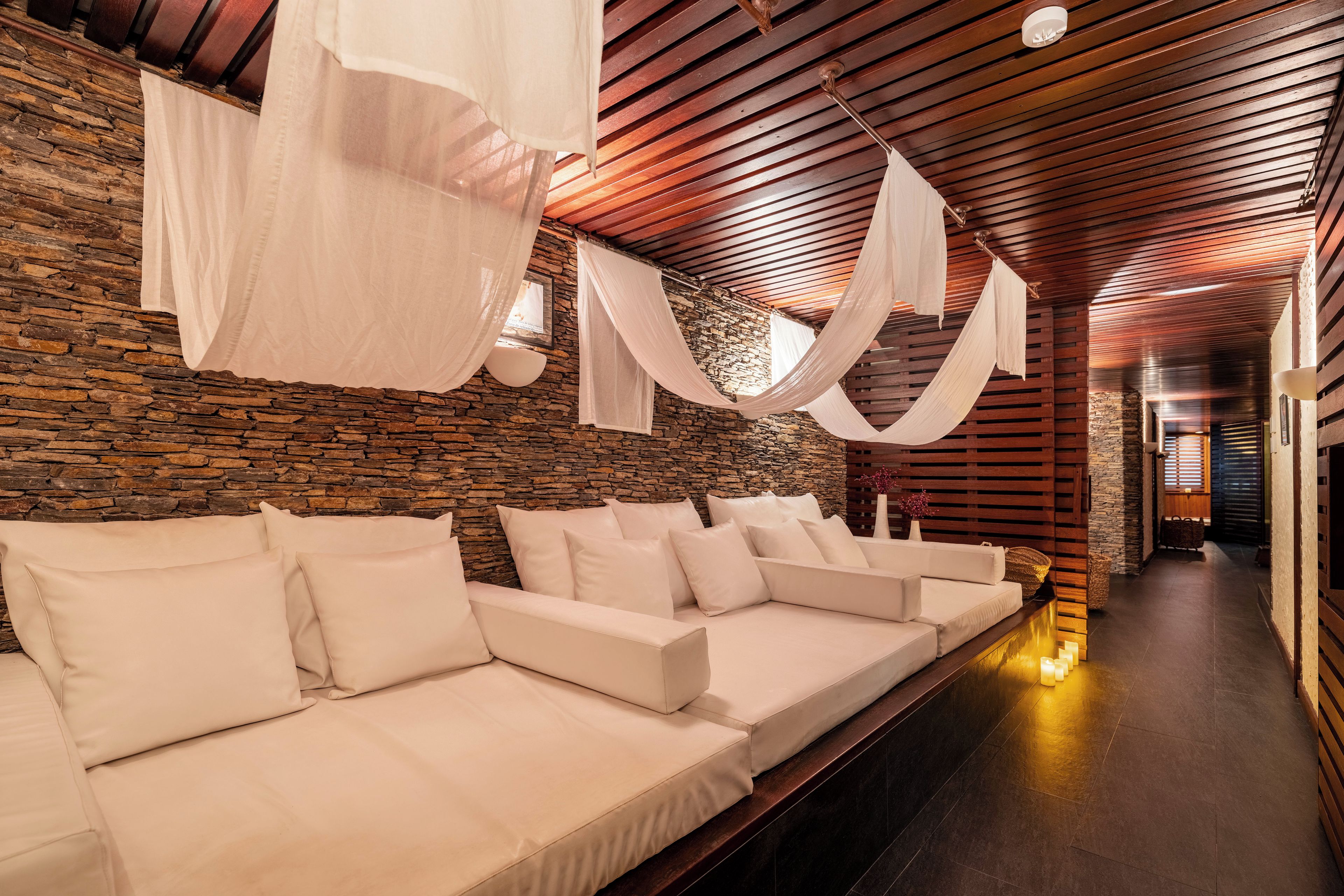 A modern interior with a stone wall, wooden ceiling, and a row of white sofas.