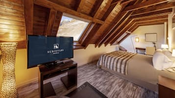 A room with a wooden ceiling, a bed, a TV, and a window with a mountain view.
