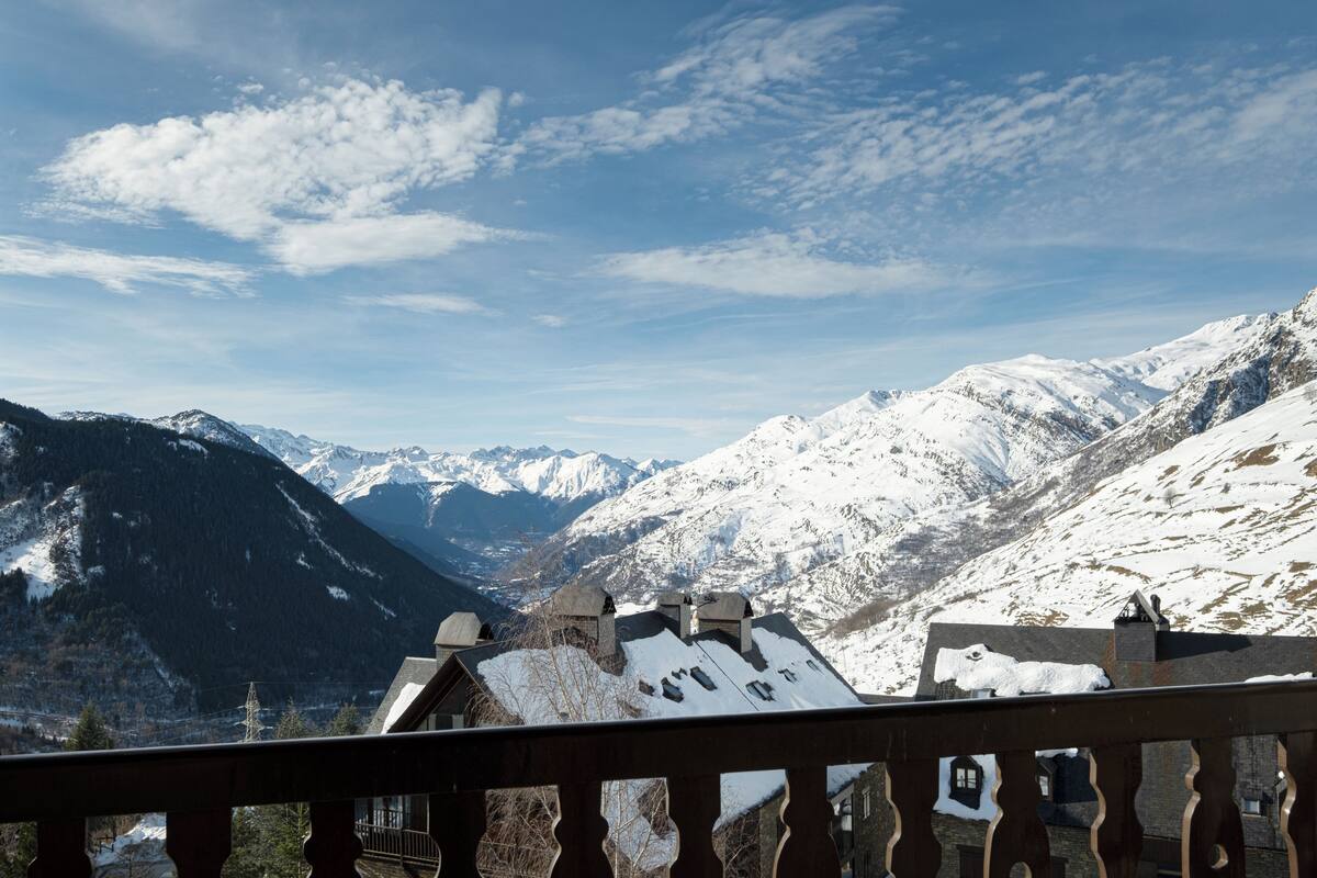 Un paysage de montagne avec des sommets enneigés et un bâtiment de style chalet doté d’un balcon en bois.