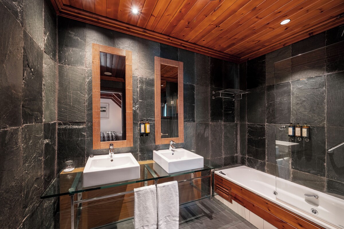 Un baño moderno con dos lavamanos, cabina de ducha de vidrio y techo de madera.
