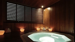 A wooden sauna room with a central hot tub, two side lamps, and a window with horizontal blinds. - Eurostars La Pleta (Naut Aran)