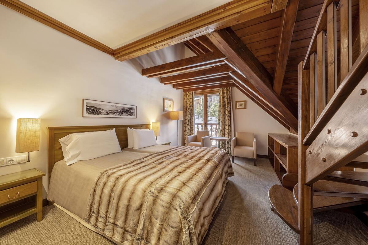 Une chambre à coucher avec un lit en bois, une table de chevet, un bureau, une chaise et un escalier.