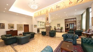 Un hall d’entrée spacieux, doté de canapés en cuir, d’une table basse et d’une fresque décorative au plafond.