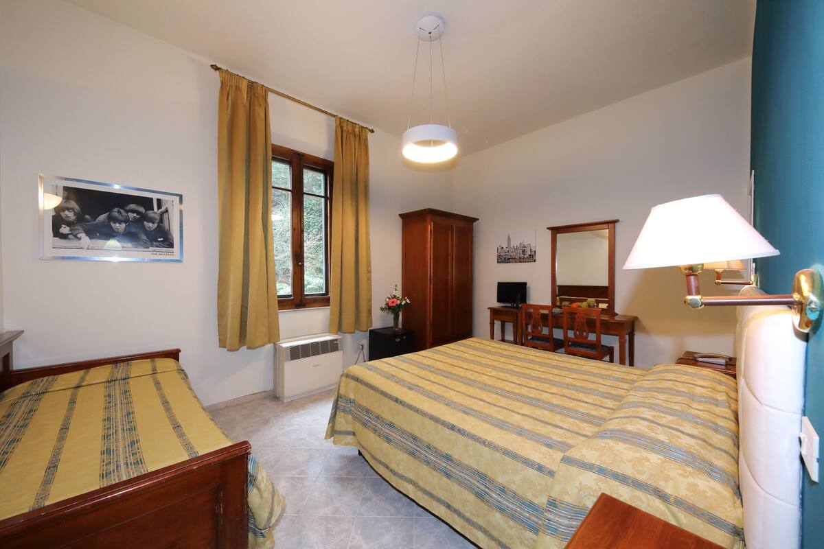 Ein Schlafzimmer mit Bett, Schreibtisch, Stuhl, Kleiderschrank und einem Fenster mit Vorhängen.