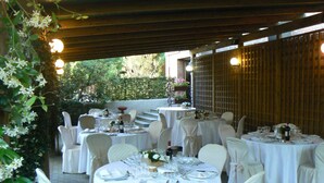 Une terrasse extérieure avec des tables rondes disposées pour les repas, entourée de chaises blanches et recouverte de nappes blanches.