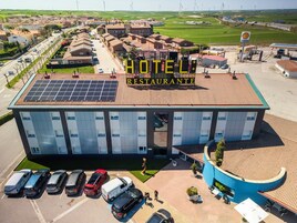 Un hotel con techo de paneles solares, un letrero de Shell y un estacionamiento con varios automóviles.