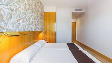 Habitación de hotel con una cama grande, cabecera de madera, panel decorativo en la pared y una puerta que da a otra habitación.