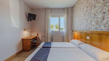 A hotel room with two beds, a desk, a TV, and a window with a view of the outside.