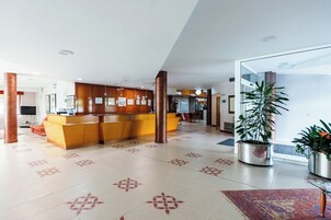 Un hall de hotel con mostrador de recepción, una planta grande en maceta y suelo estampado.